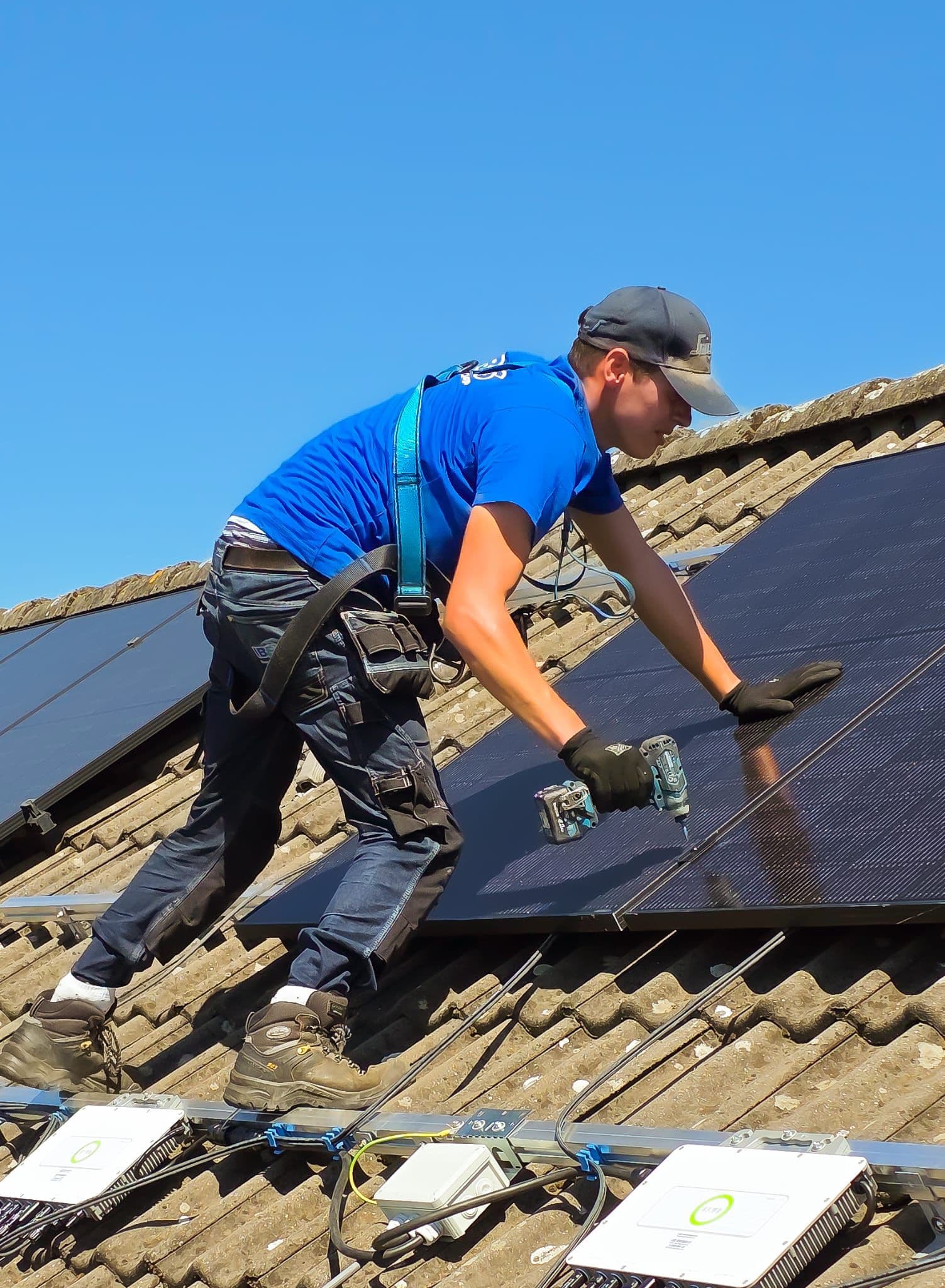 Een man met veiligheidsharnas monteert zonnepanelen op een pannendak.